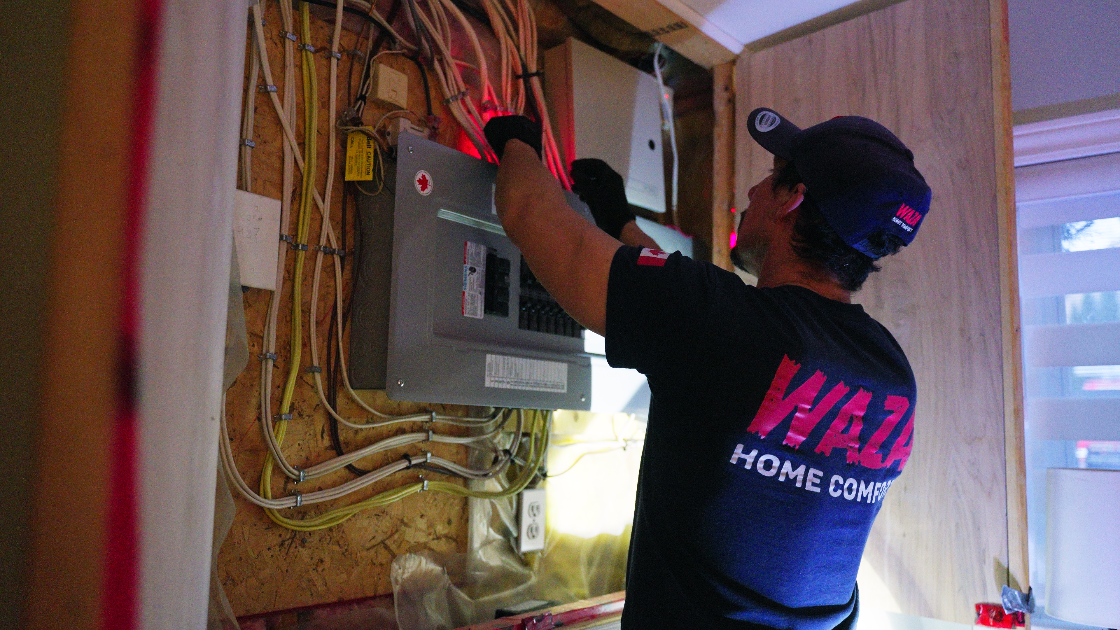 A WAZA Home Comfort technician working on an electrical panel during an installation